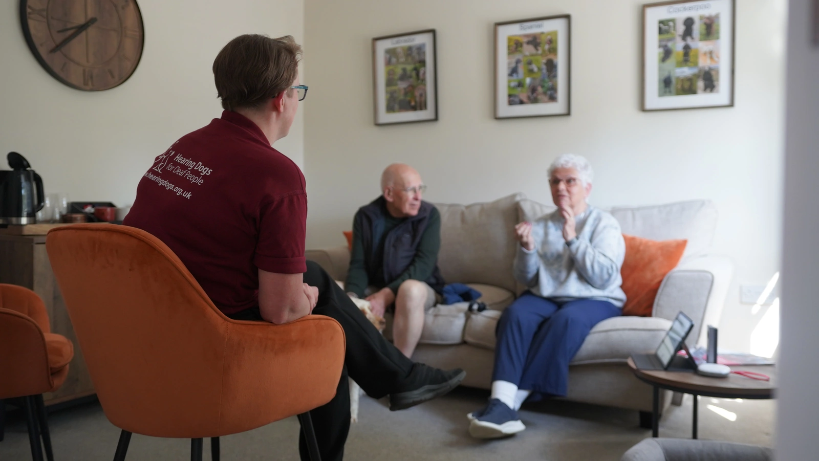A man and woman in conversation seen from over the shoulder of a woman in hearing dogs staff uniform