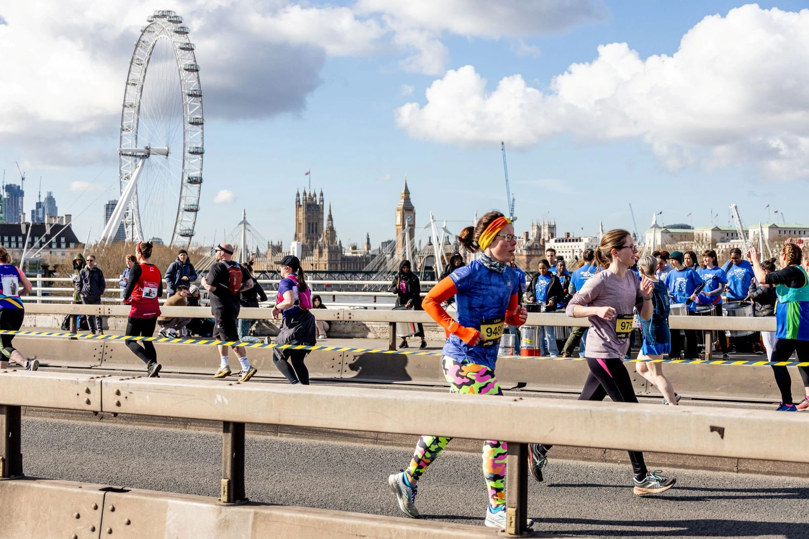 A group of marathon runners on a road. The London Eye big wheel can be seen in the background