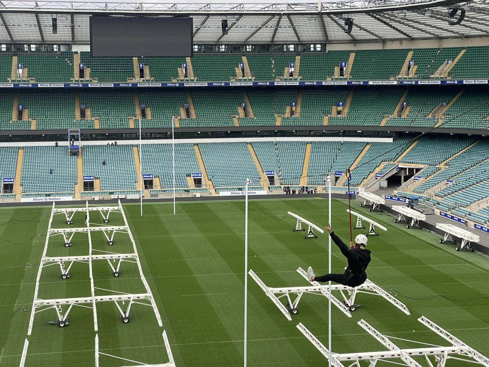 A view from high up in a large sports stadium, of a woman in black, ziplining across the pitch.