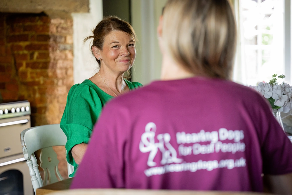 A woman, Karen, seen over the shoulder of another person wearing a hearing dogs staff uniform. Karen is smiling slightly.