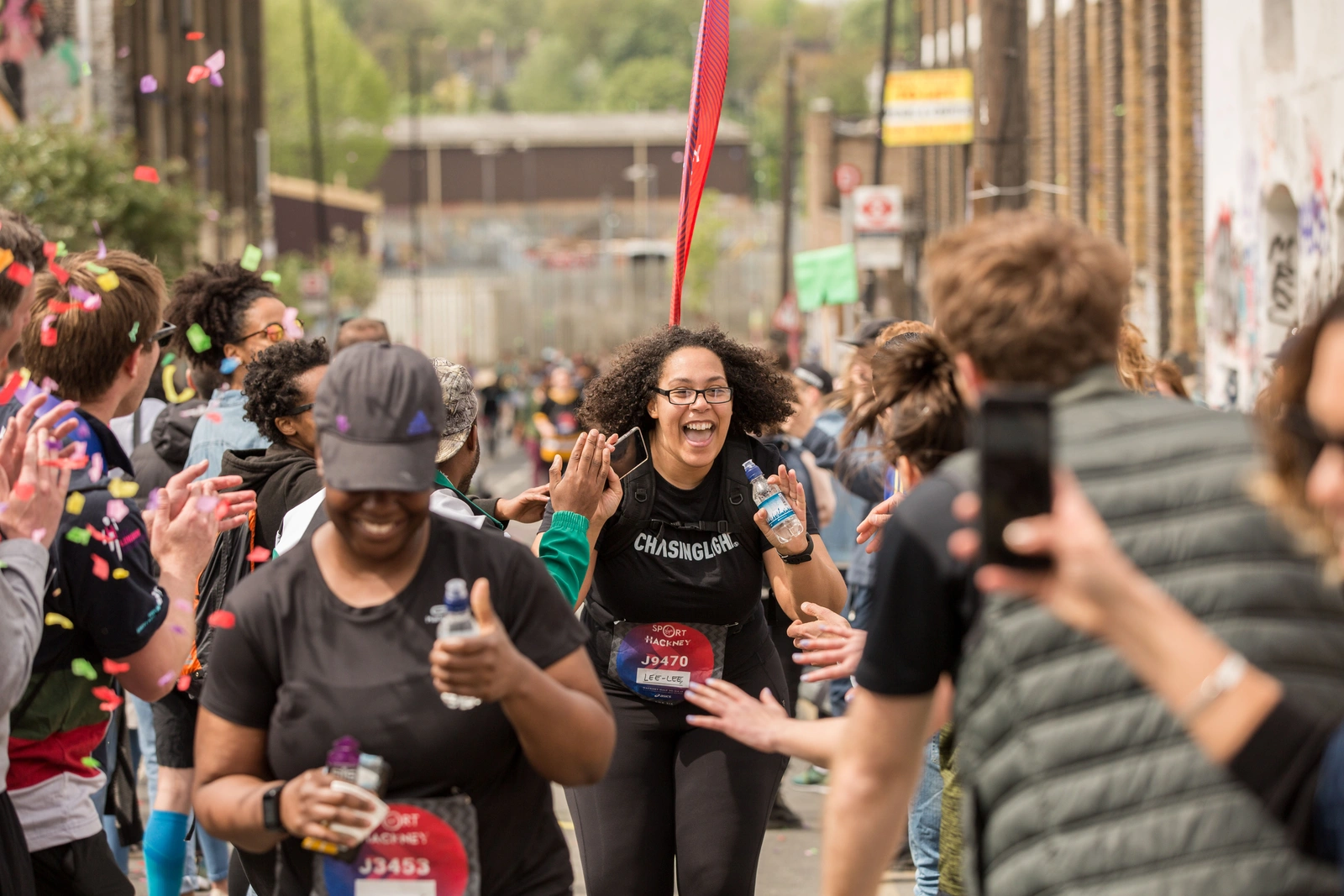 Runners take part in the Hackney Half Marathon as spectators line the route, cheering and offering high-fives while confetti falls around the course.
