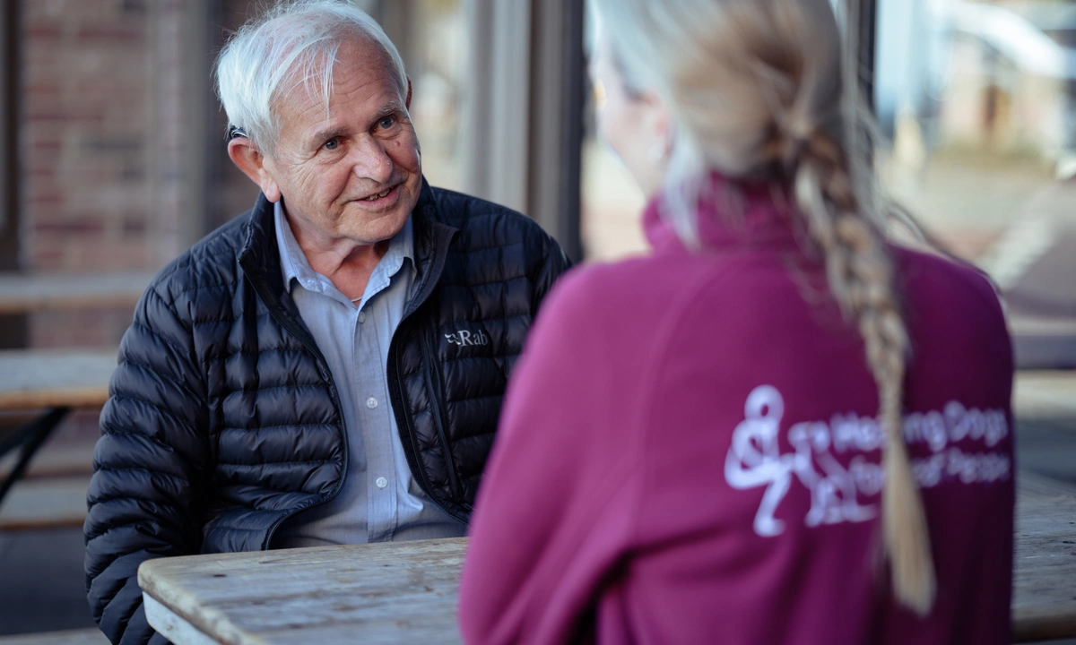 David is sitting a picnic table chatting with a woman wearing a hearing dogs uniform