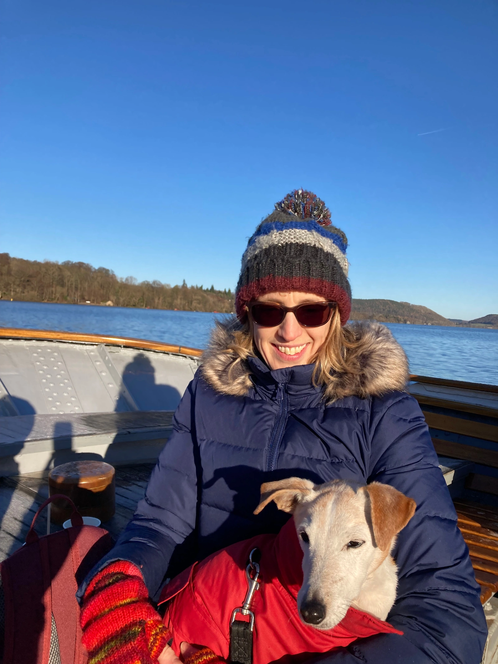 A woman wearing a beanie hat and sunglasses, holding a dog in her lap