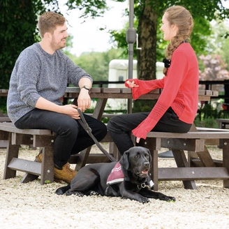 Two people sat on a bench outside chatting, one of them had a hearing dog wearing a qualified jacket